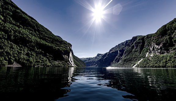 Norweski fiord z wodospadami spływającymi z zielonych gór w słoneczny dzień.