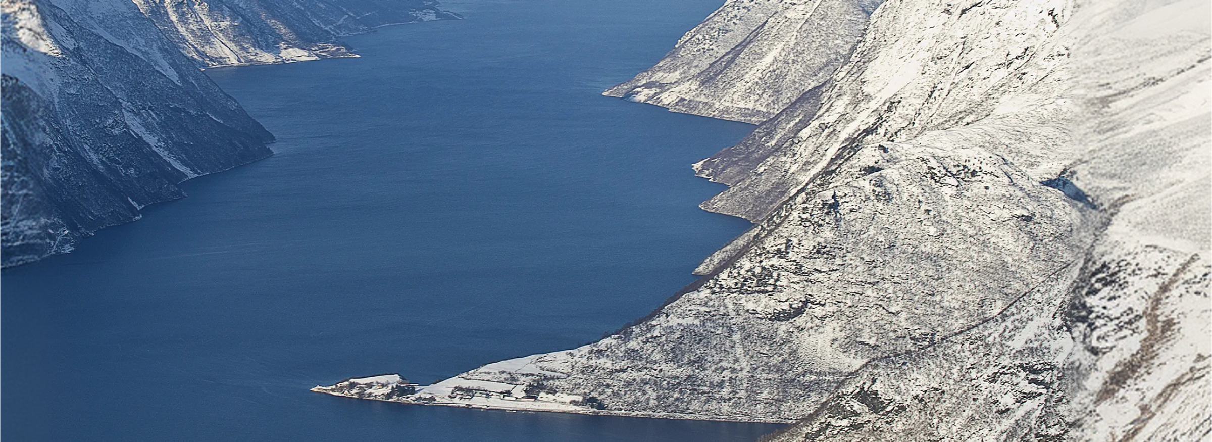 Widok z lotu ptaka na norweski fiord otoczony ośnieżonymi, stromymi górami.