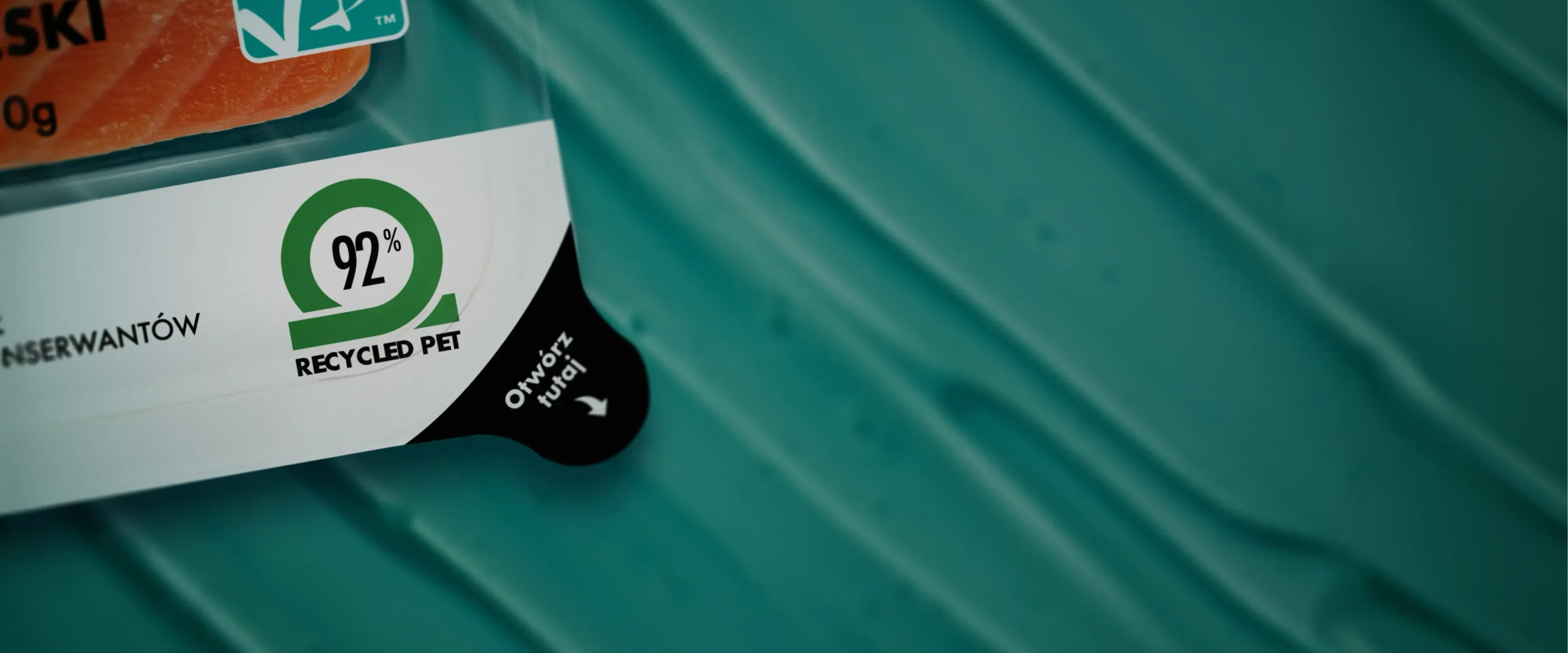Etykieta opakowania łososia informująca o 92% zawartości przetworzonego plastiku oraz o miejscu otwarcia.